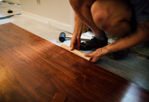 Faceless male master laying wooden laminate flooring using mallet in apartment during renovation
